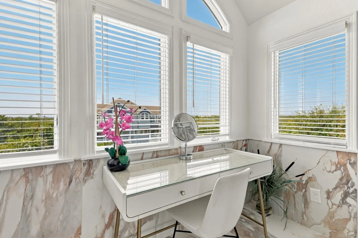 A bright vanity area sits beside large windows with white blinds.