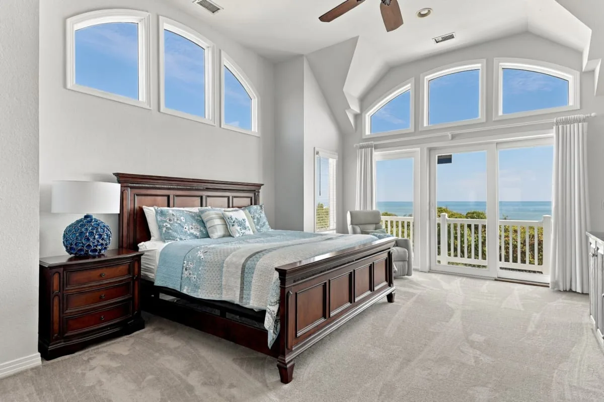 A bright bedroom with a large bed facing windows and glass doors overlooking the water.