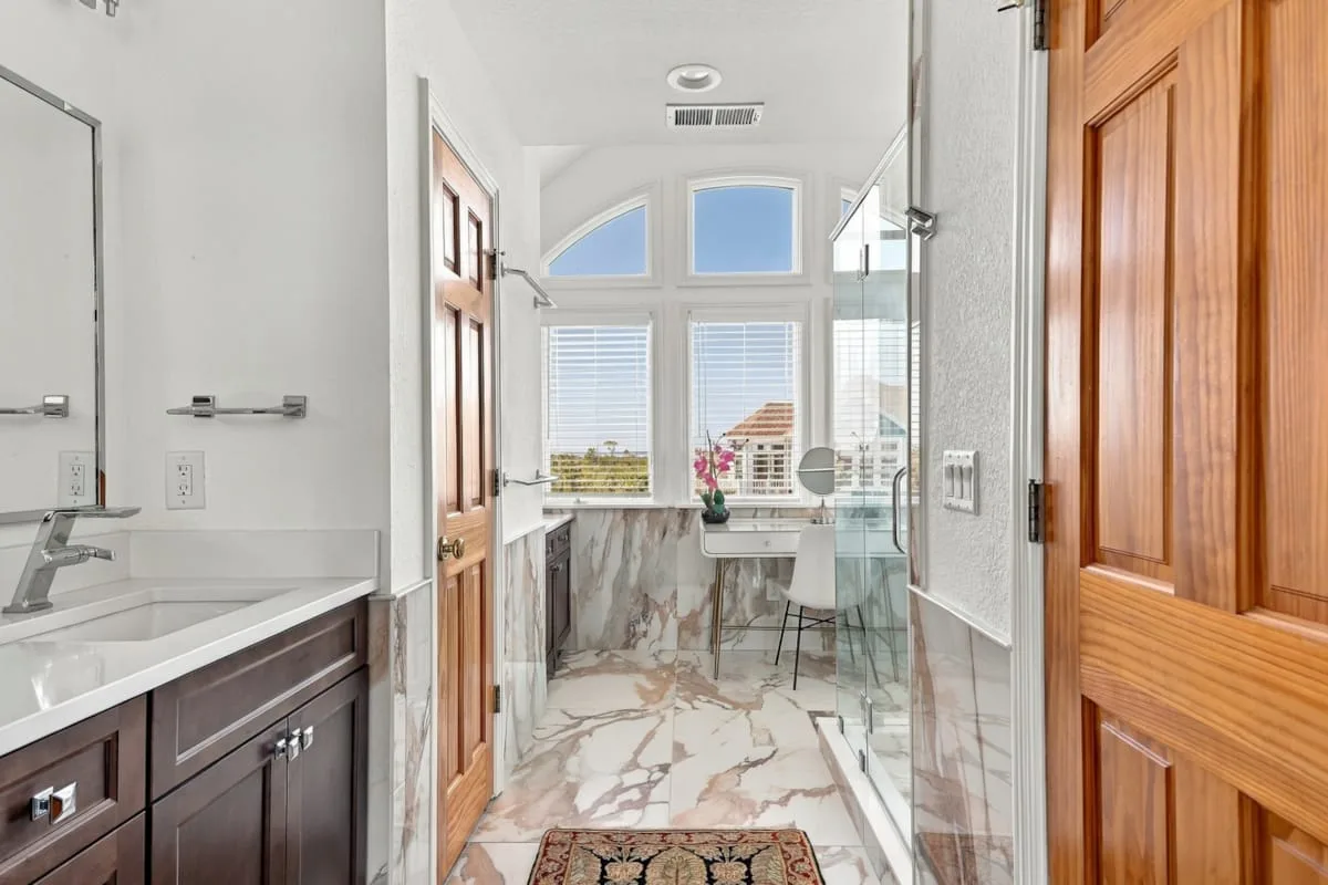 A bright bathroom with a vanity, large windows, and a glass shower.