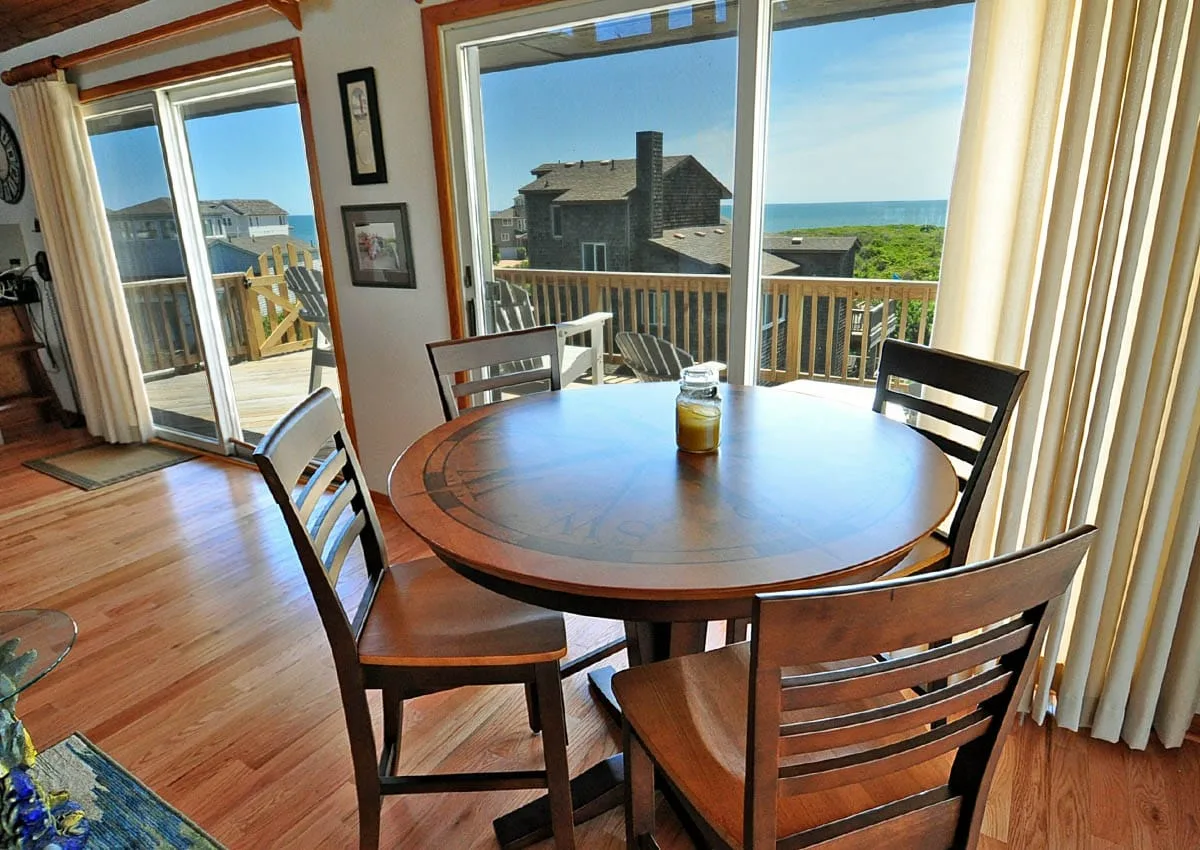 Comedor con una mesa redonda de madera junto a grandes ventanas con vista a la costa.