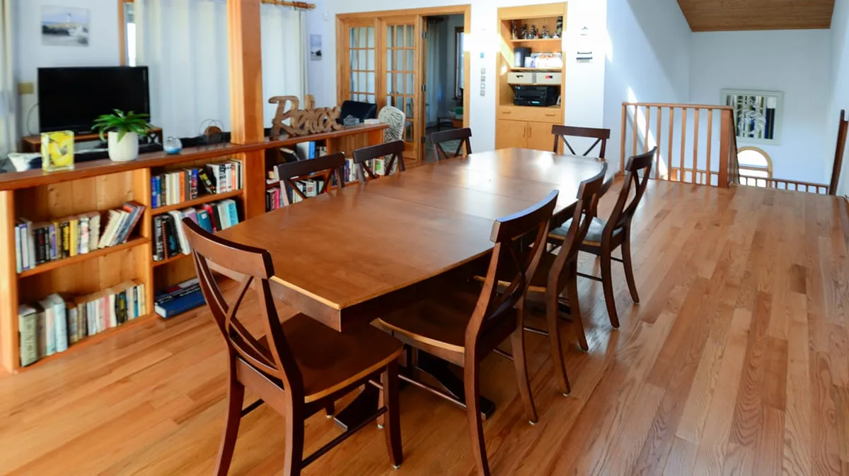 A dining area with a long wooden table and bookshelves along the wall.