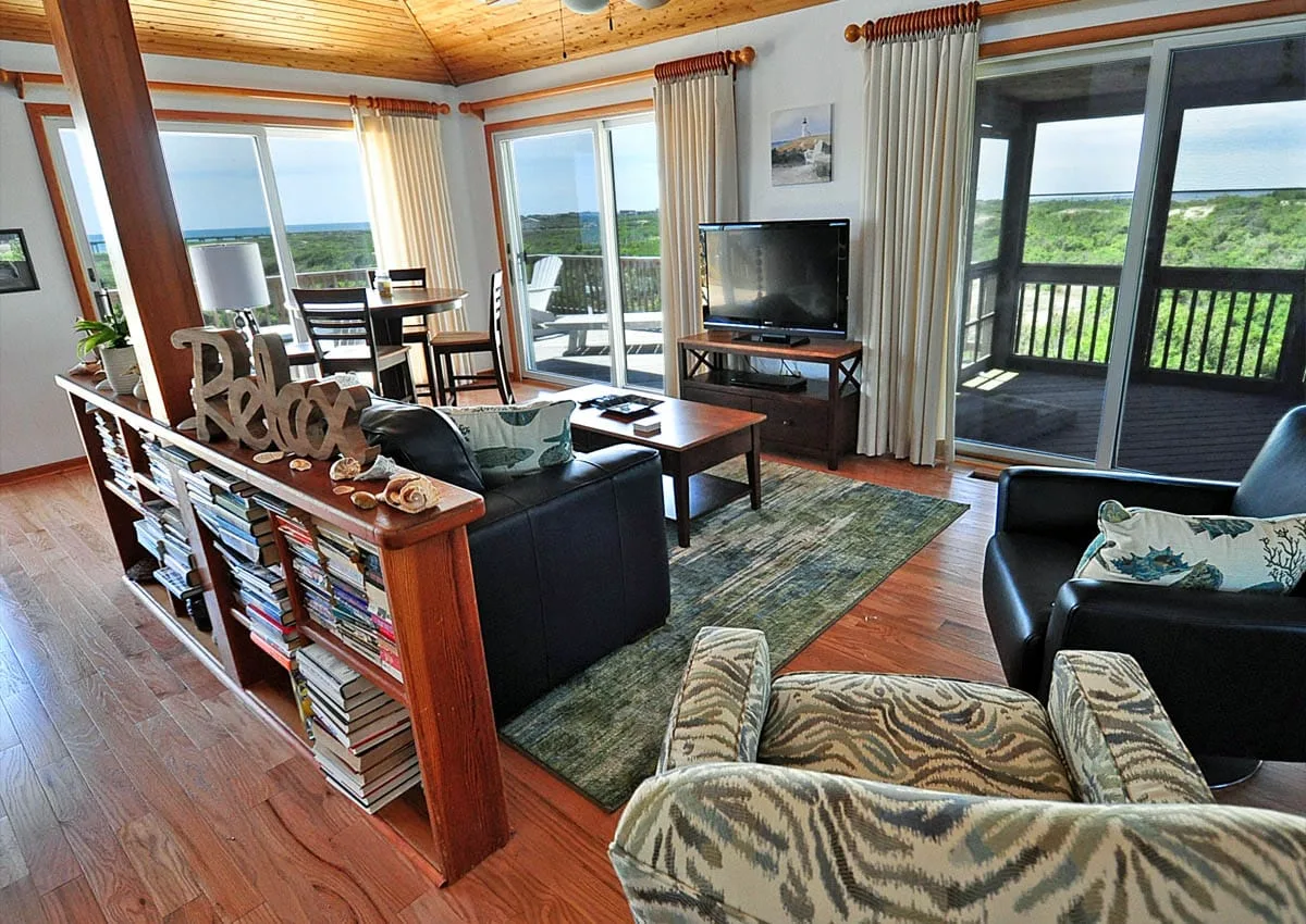 A living room with seating, a television, and large windows overlooking a deck.