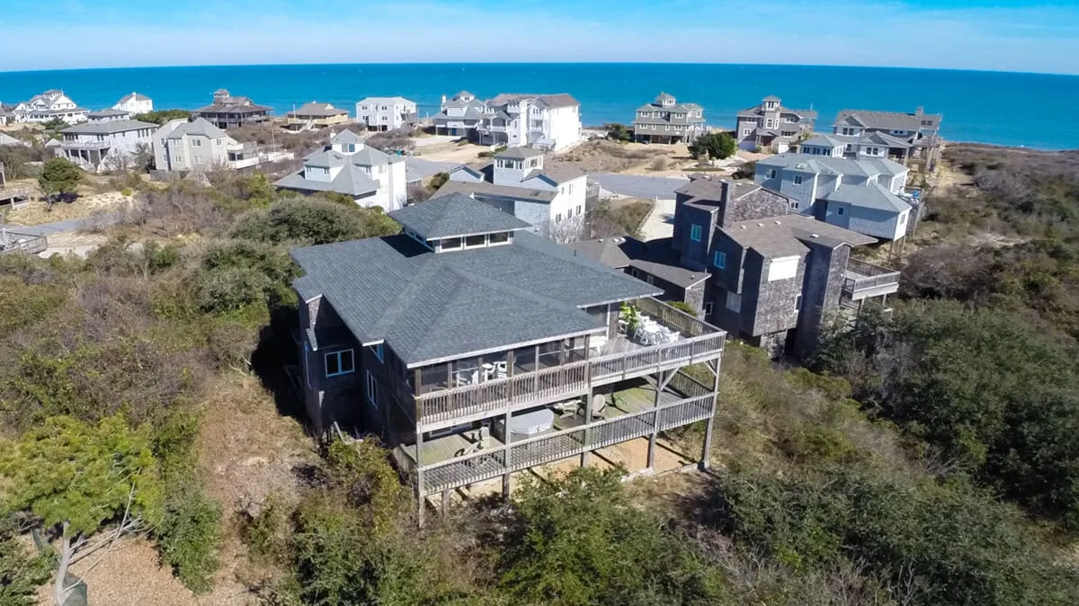 Aerial view of coastal houses among low vegetation beside the ocean.