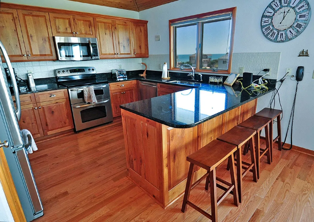A kitchen with wooden cabinetry, dark countertops, and a central island with seating.