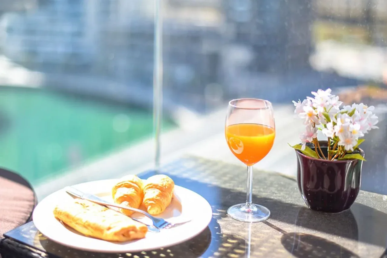 A breakfast plate with pastries, orange juice, and flowers sits by a bright window.