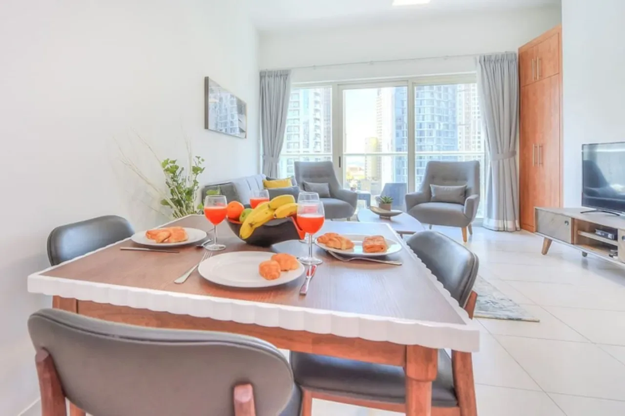 A dining table set with food sits beside a bright living area with large windows.