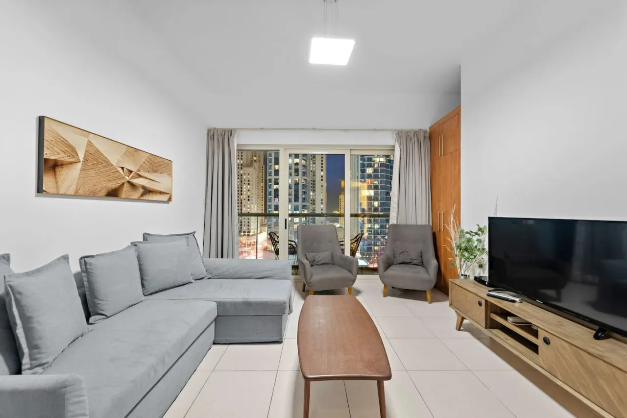 A bright living room with gray seating, a wooden coffee table, and large windows.