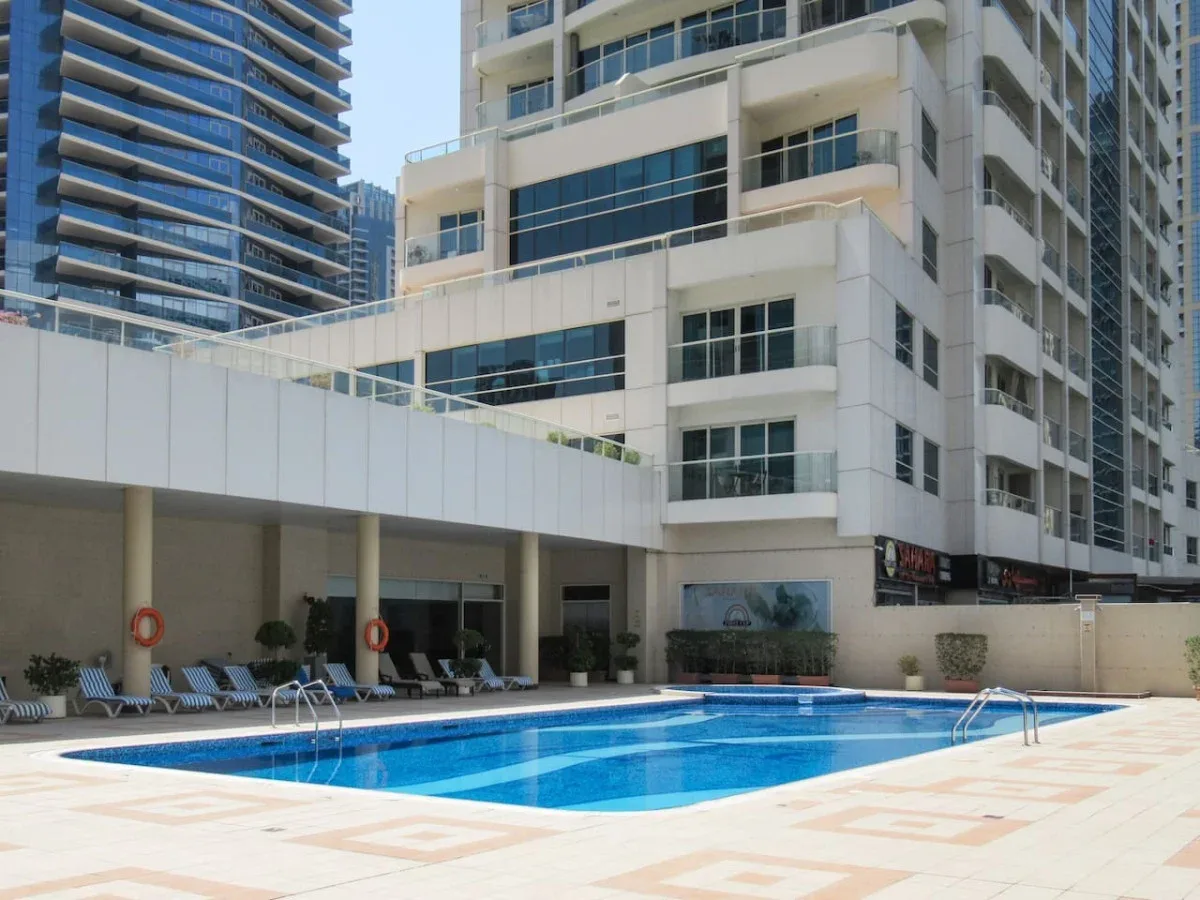 An outdoor swimming pool sits beside a modern multi-story building.