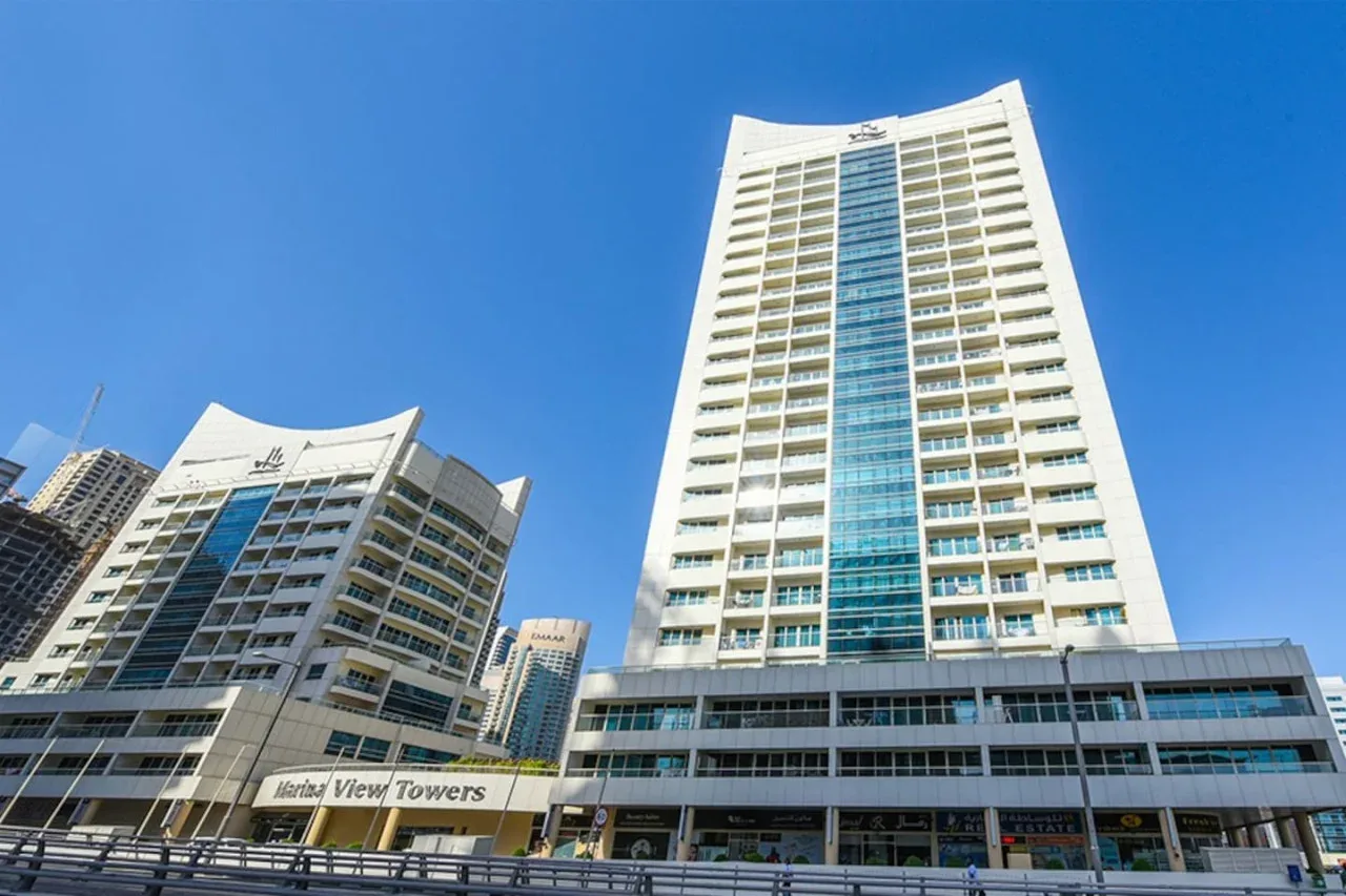 A tall modern building with a blue glass center rises against a clear sky.