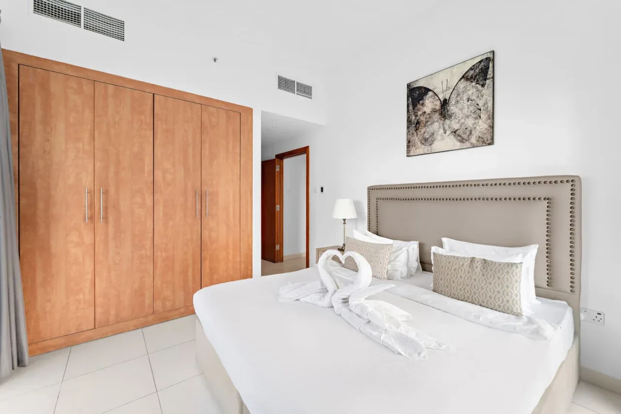 A bright bedroom with a neatly made bed and built-in wooden wardrobes.