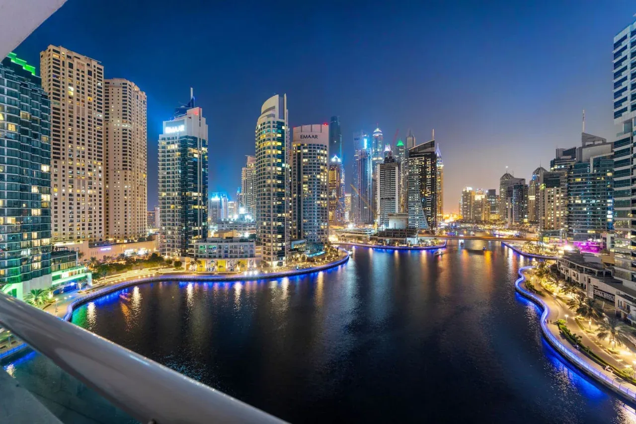 A nighttime city skyline reflects across a waterfront lined with illuminated buildings.