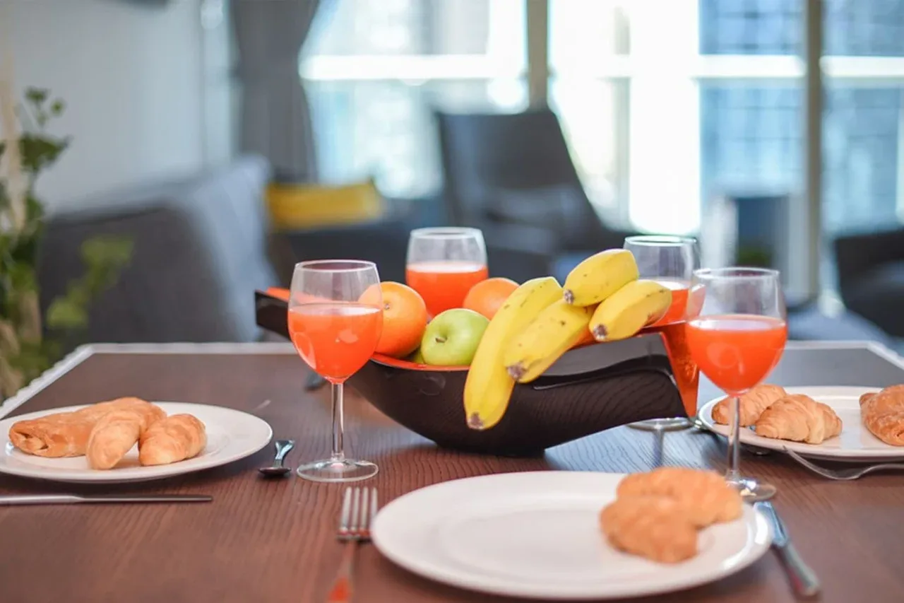 A dining table is set with fruit, pastries, plates, and glasses of juice.