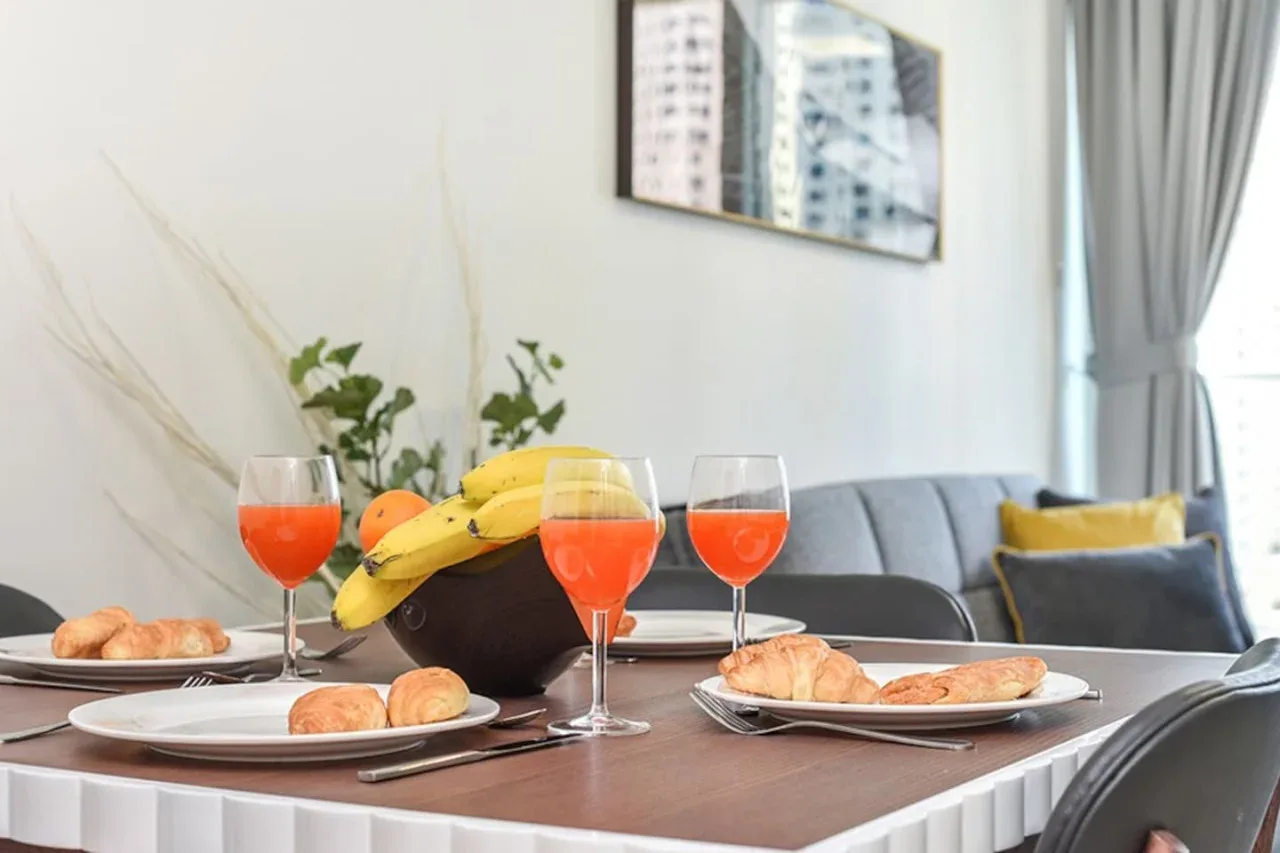 A dining table is set with plates, pastries, fruit, and glasses in a living room.