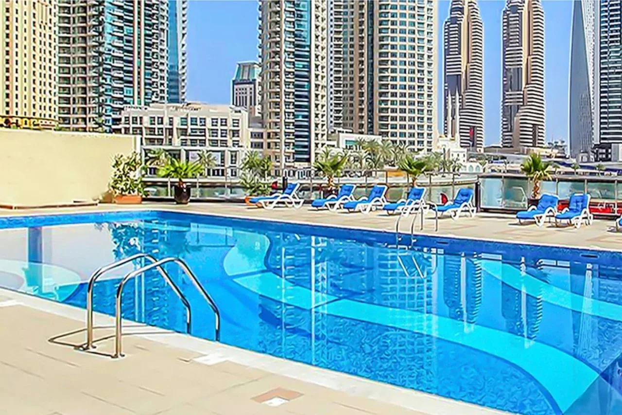 A rooftop swimming pool with lounge chairs and tall buildings in the background.