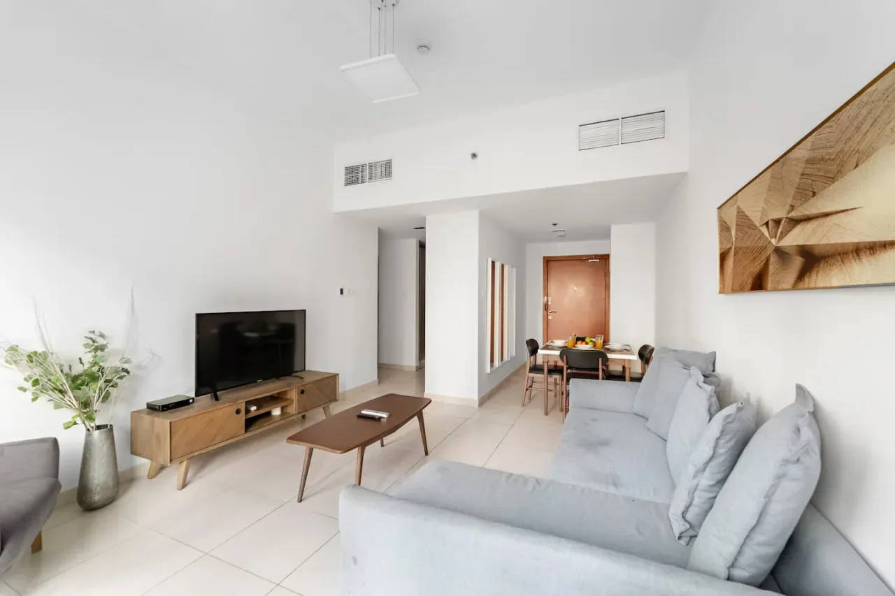 A bright living room with pale seating, a television, and a wooden coffee table.
