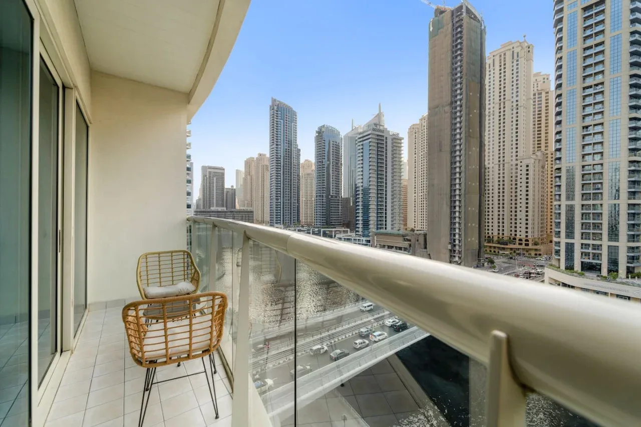 A balcony with glass railings overlooks a canal and a cluster of high-rise buildings.