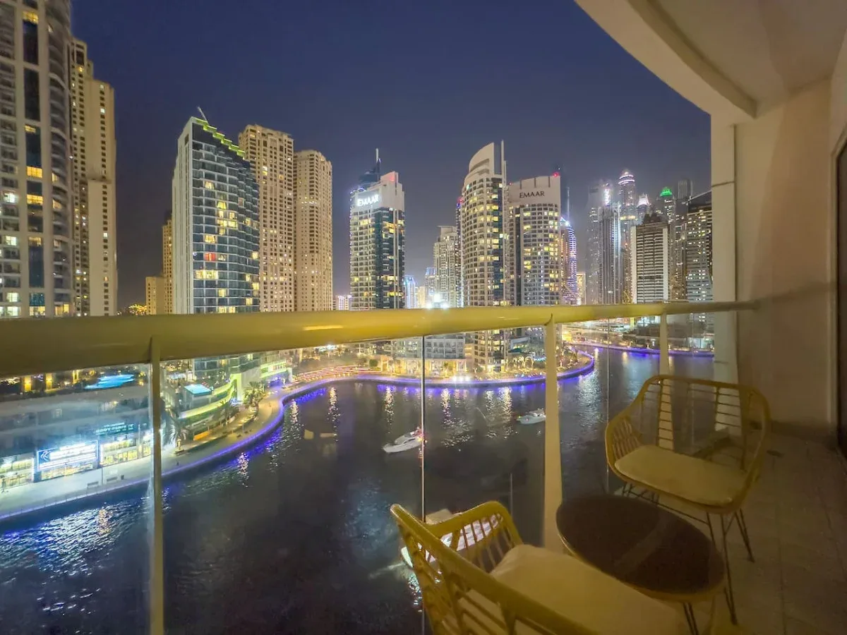 A balcony overlooks a waterfront canal and illuminated city skyline at night.
