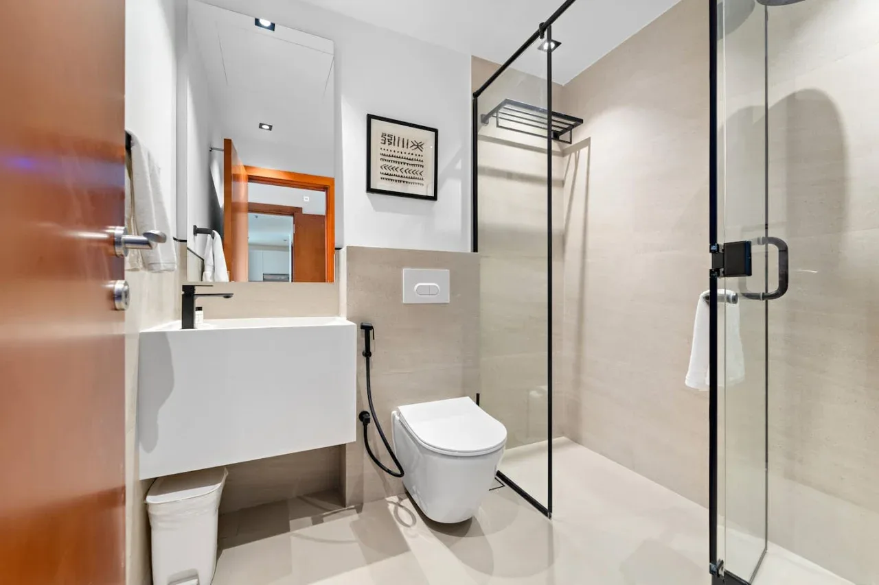A modern bathroom with a wall-mounted sink, toilet, and glass shower.