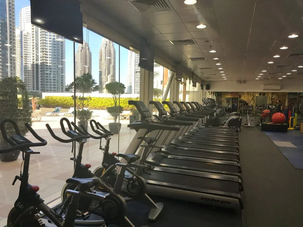 A gym lined with treadmills and stationary bikes beside large windows.