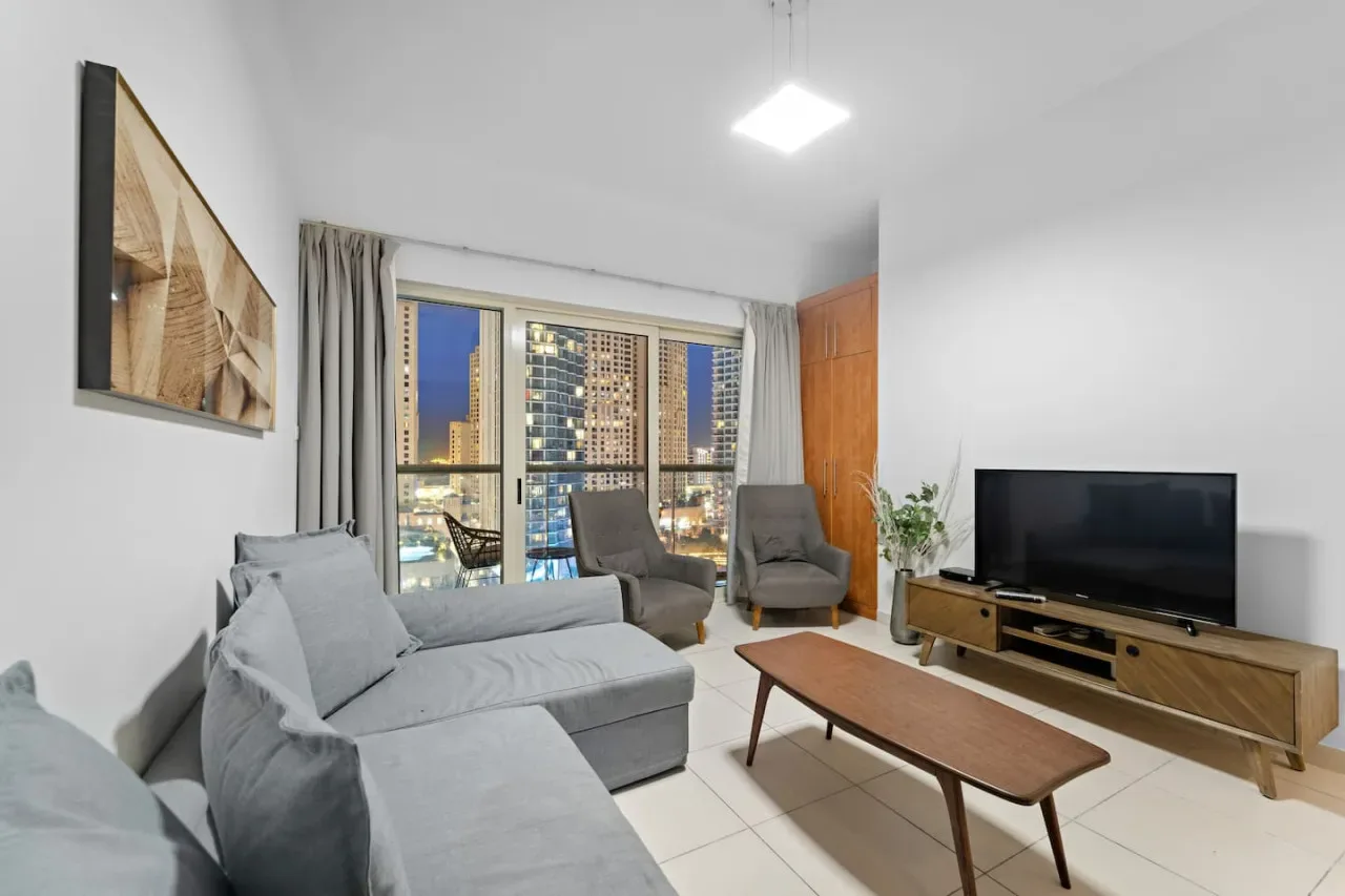 A living room with seating, a television, and large windows overlooking city lights.