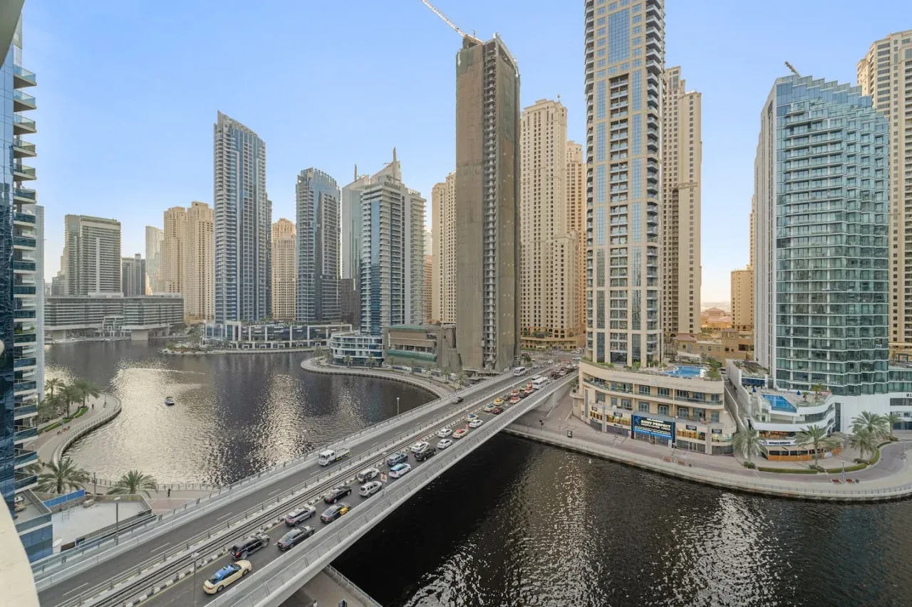A city waterfront skyline with tall buildings, a canal, and a bridge.