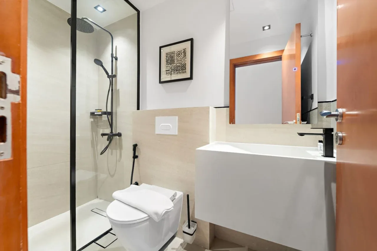 A modern bathroom with a glass shower, toilet, and white vanity.