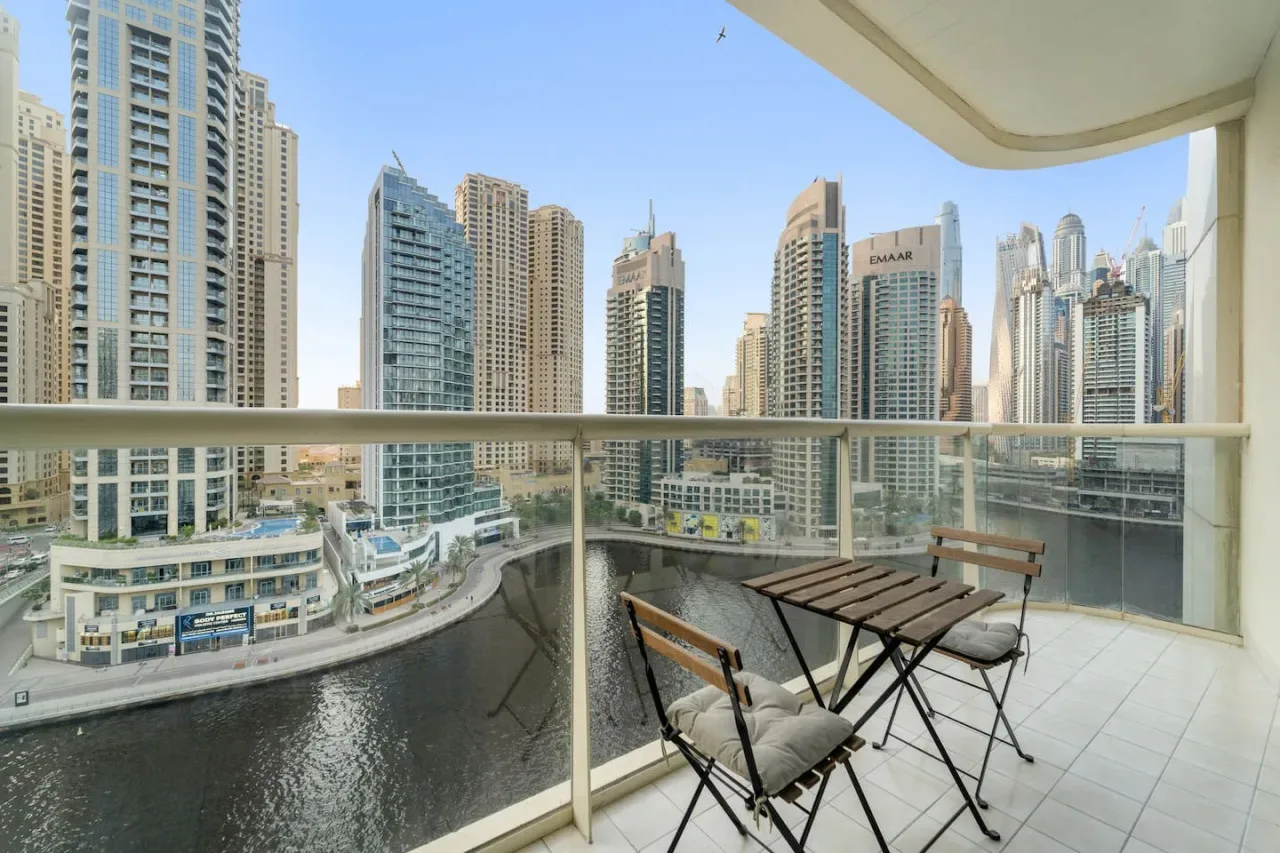 A balcony seating area overlooks a canal and a cluster of high-rise buildings.