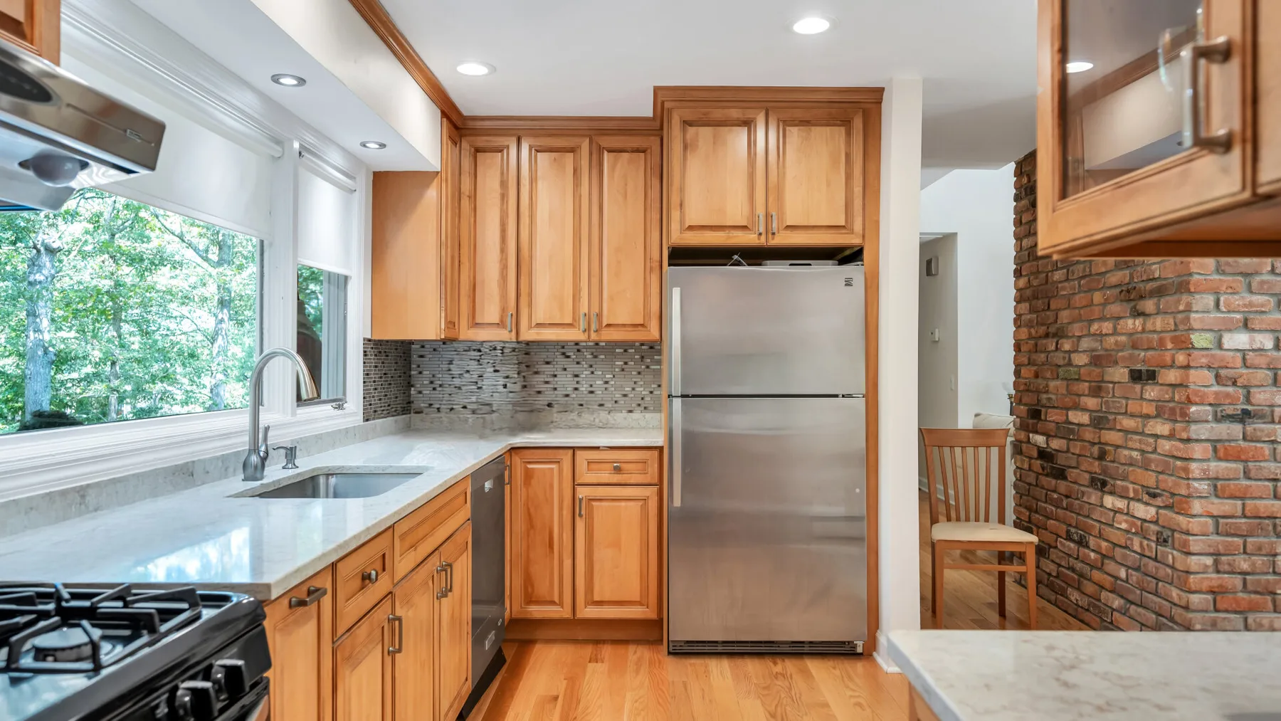 Una cocina con gabinetes de madera, un refrigerador de acero inoxidable y una pared de ladrillo.