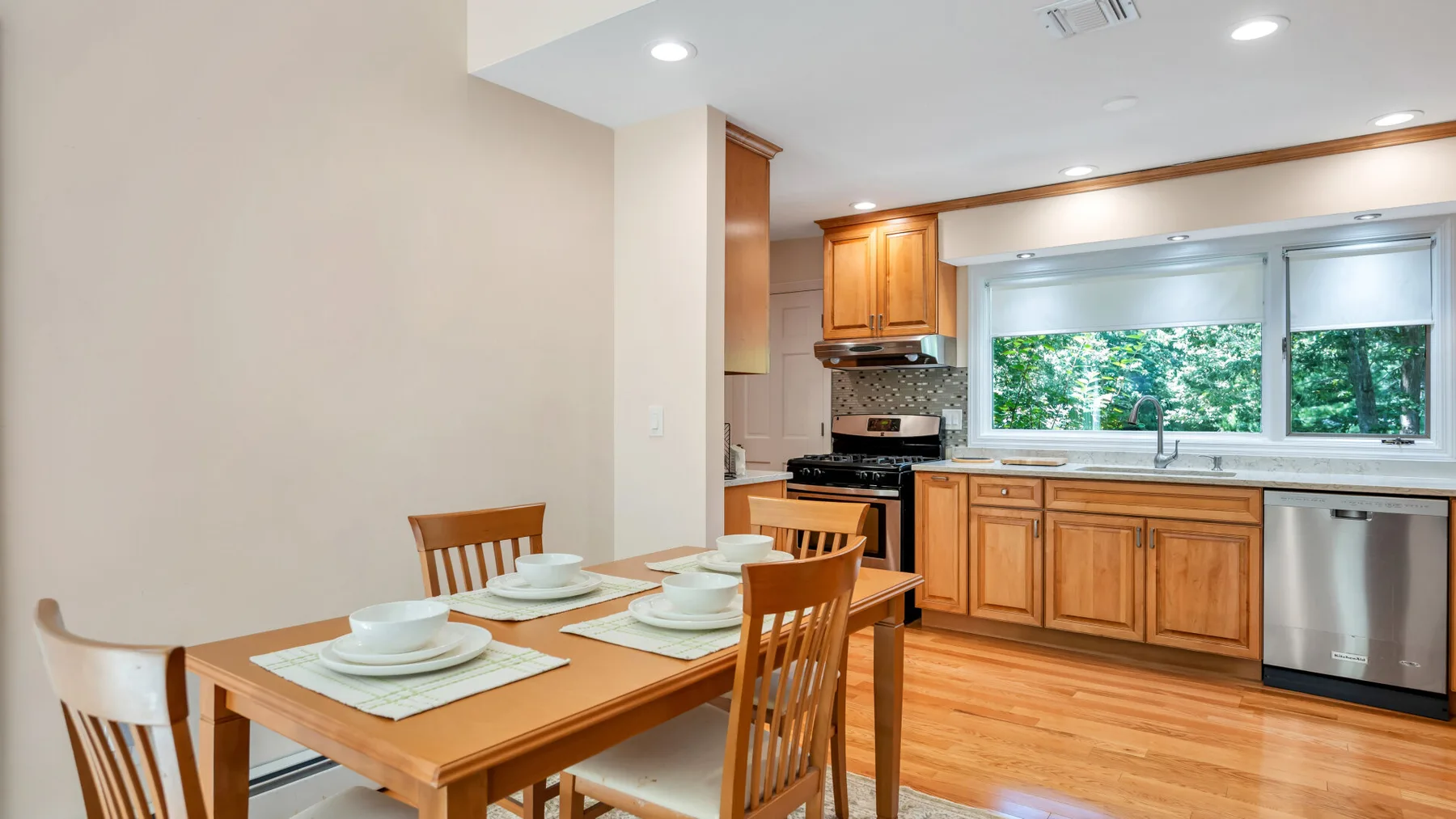 Un comedor se conecta con una cocina con gabinetes de madera y una ventana amplia.