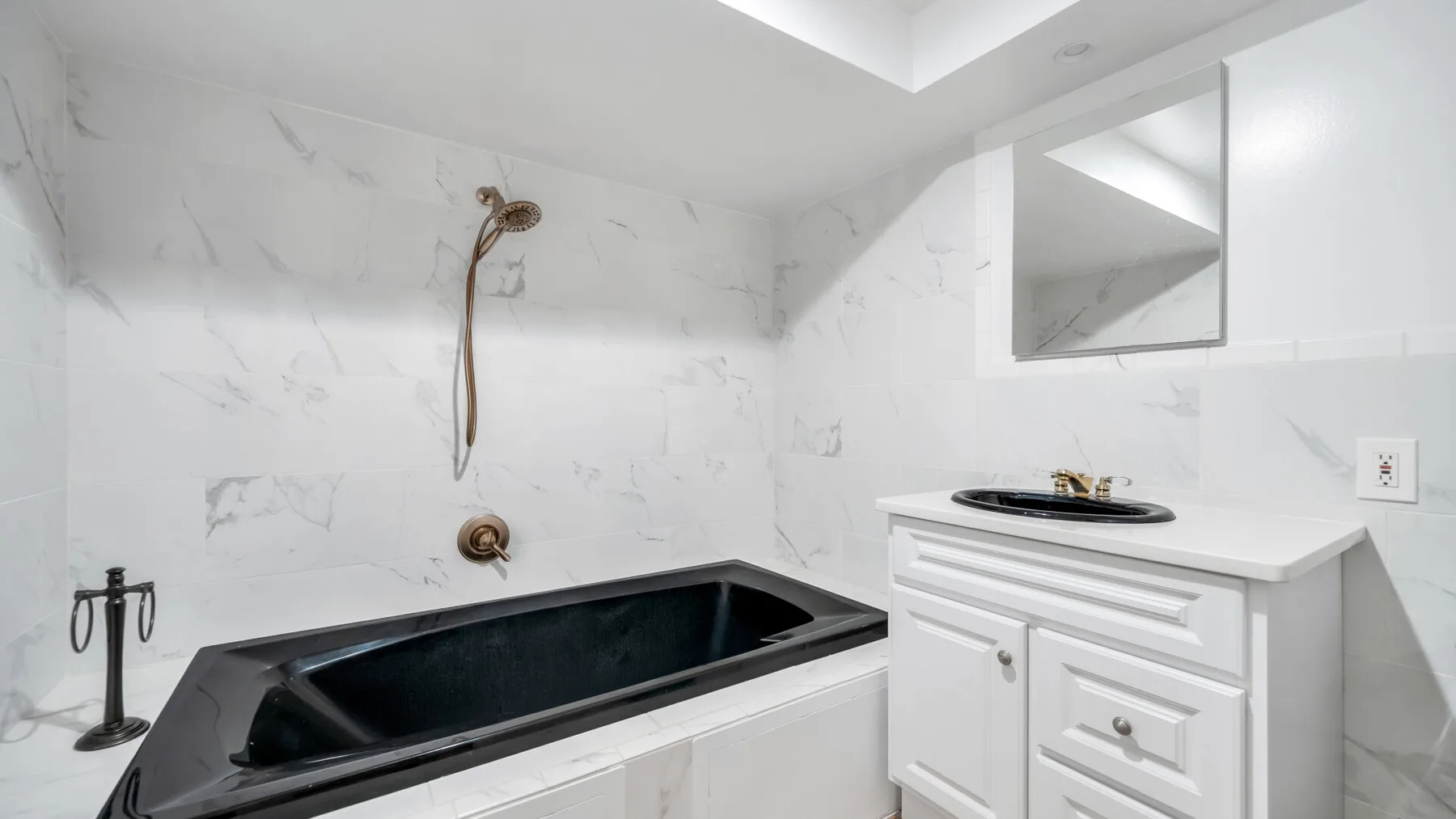 Un baño con una bañera oscura y un tocador blanco.
