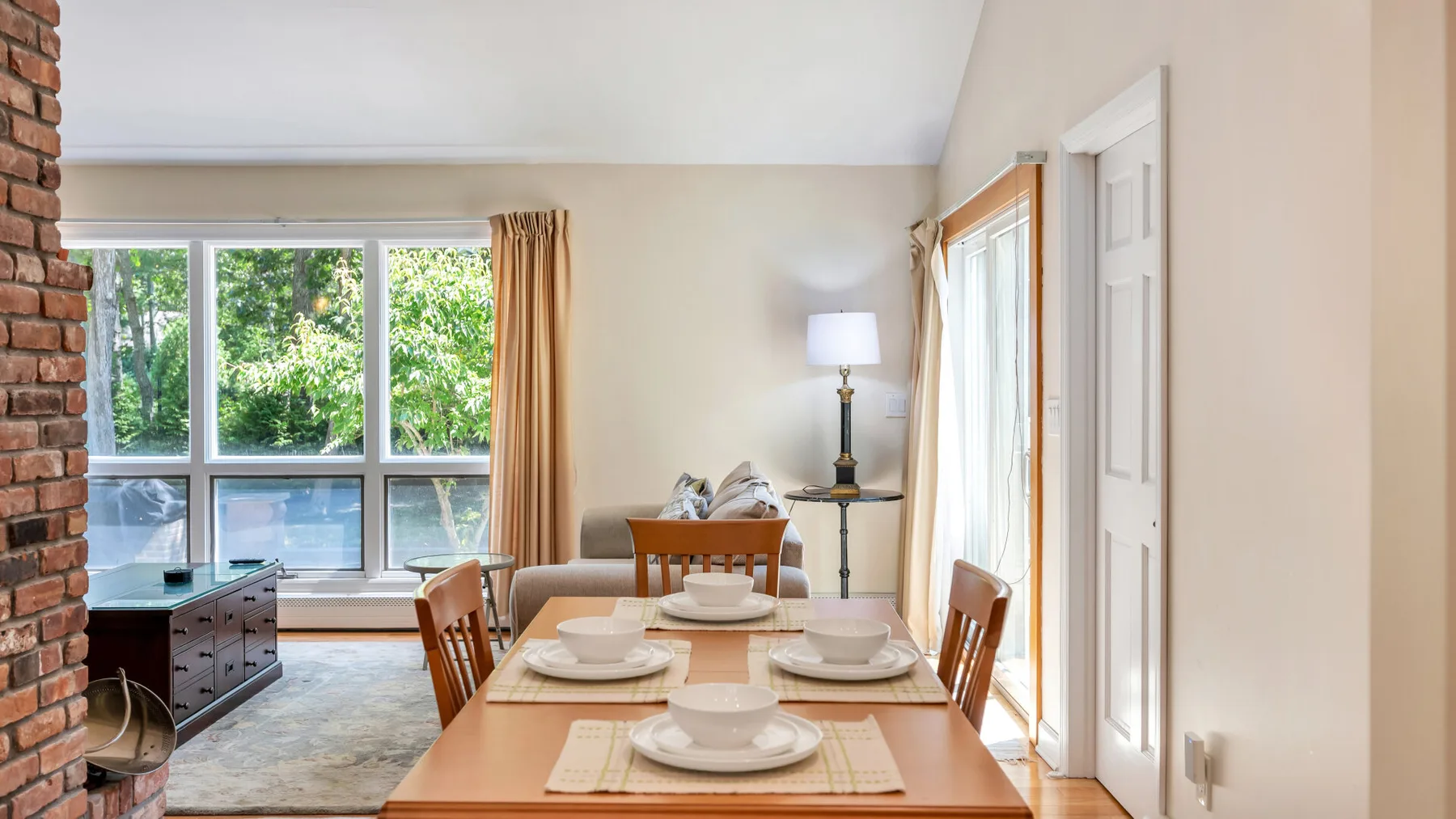 Un comedor con la mesa puesta junto a grandes ventanas con vistas a la vegetación.