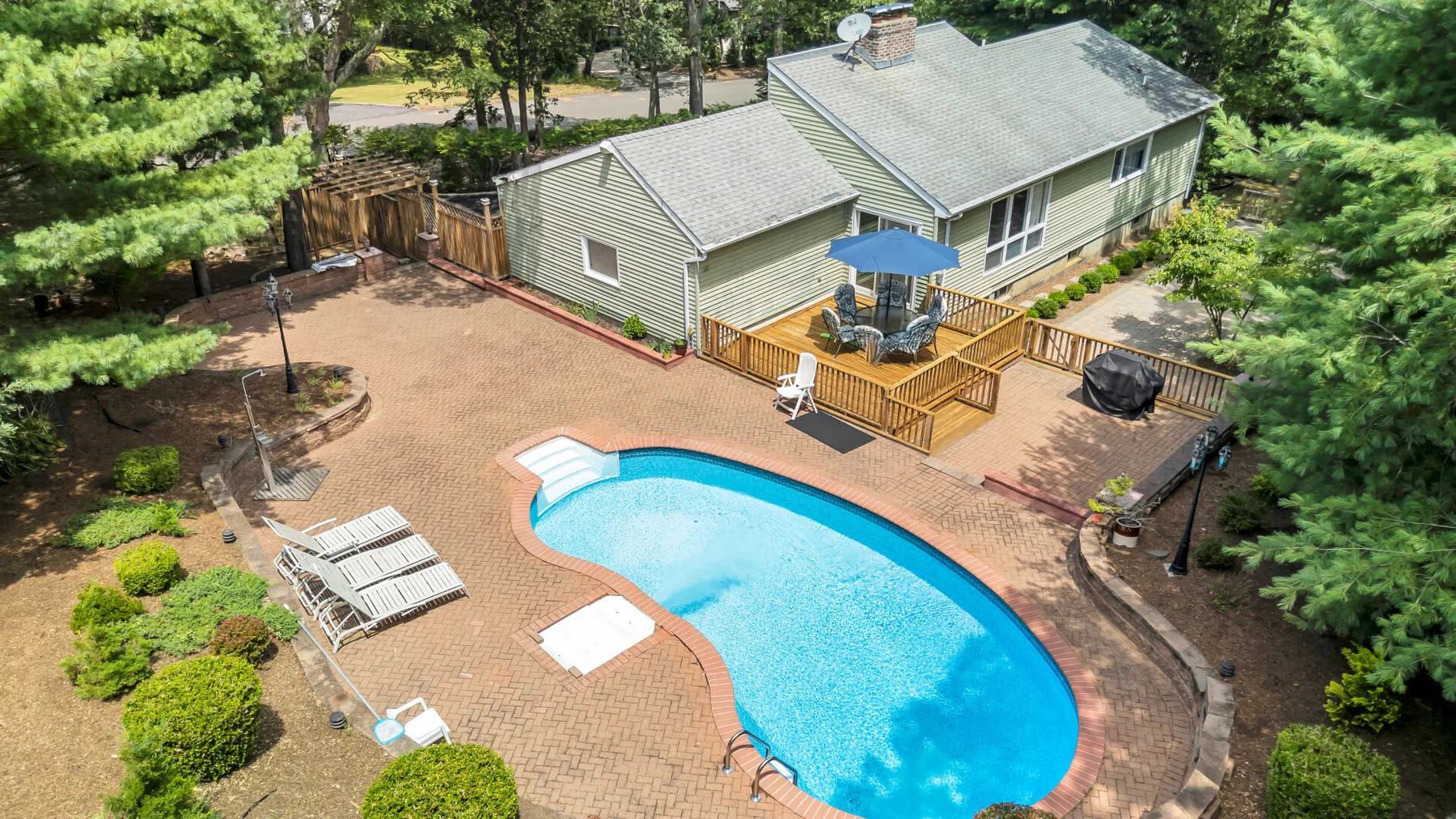 Una casa con piscina y una terraza de madera en un jardín ajardinado.