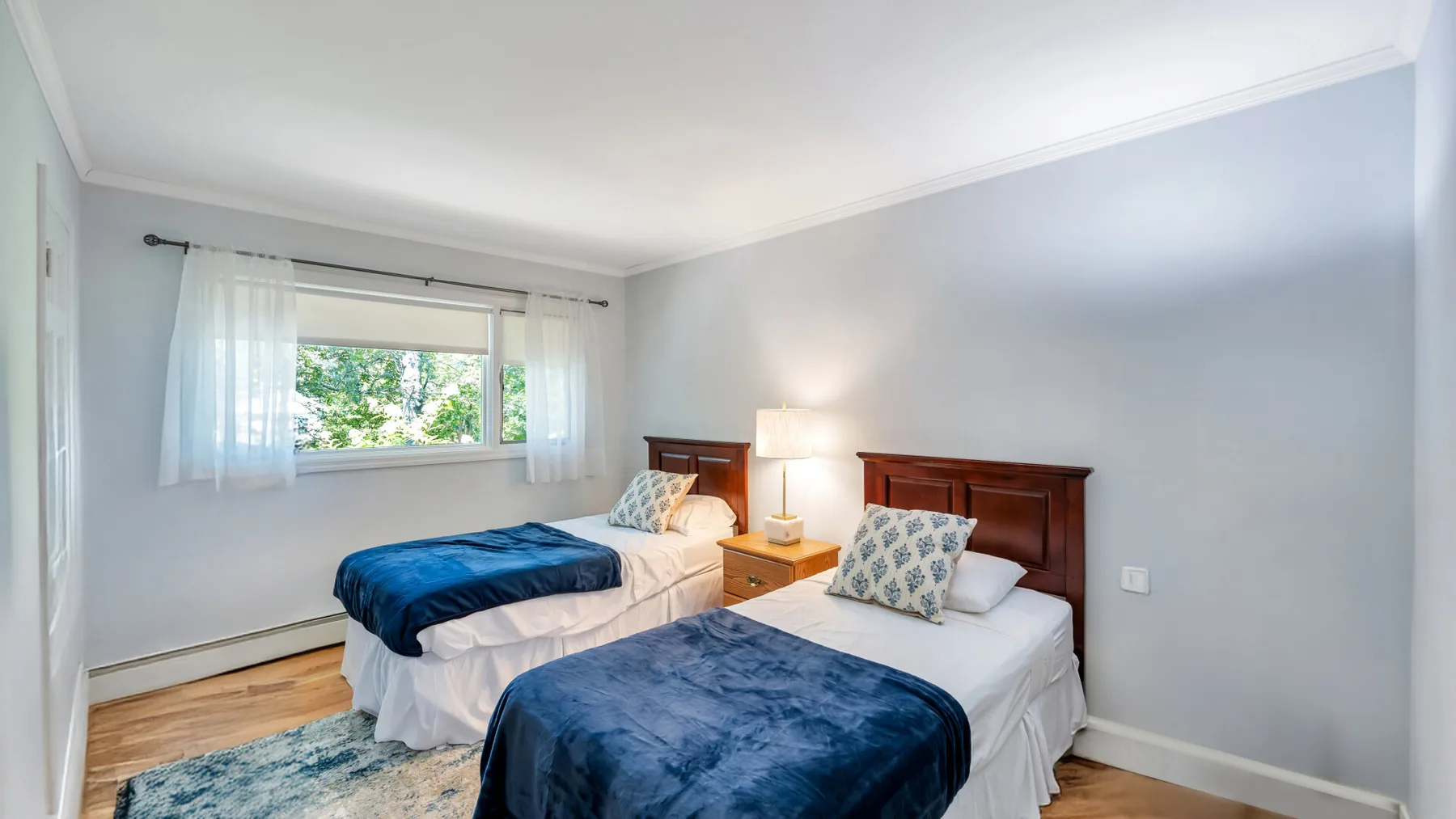 Un dormitorio con dos camas junto a una ventana con cortinas transparentes.
