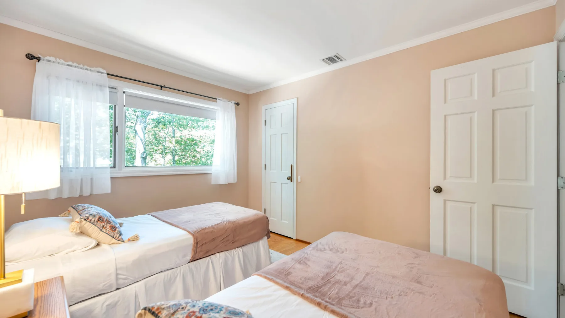 Un dormitorio con dos camas, una ventana y cortinas blancas.