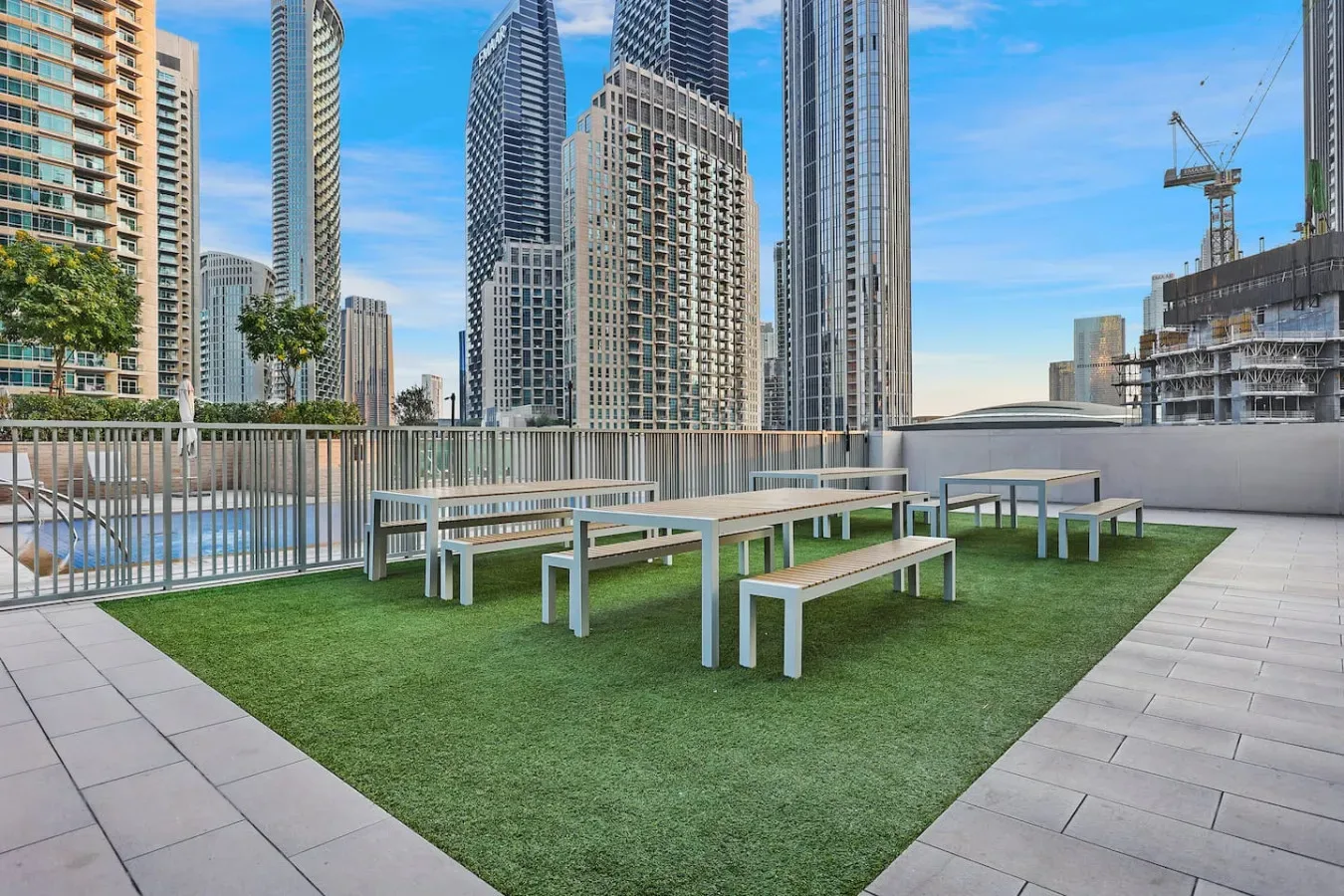 Una terraza en la azotea tiene asientos al aire libre sobre césped artificial, con edificios de la ciudad al fondo.