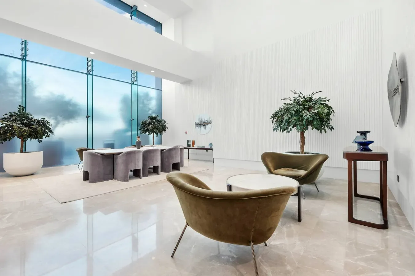 Un salón moderno y luminoso con asientos alrededor de una mesa baja y ventanas altas.