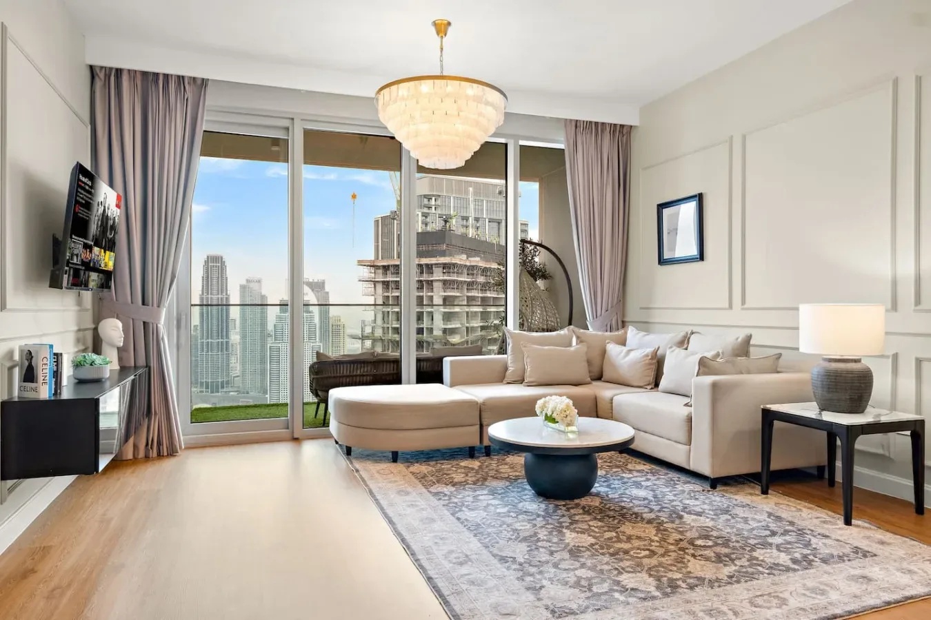 Una sala luminosa con sofá seccional y grandes ventanales con vista a edificios de la ciudad.