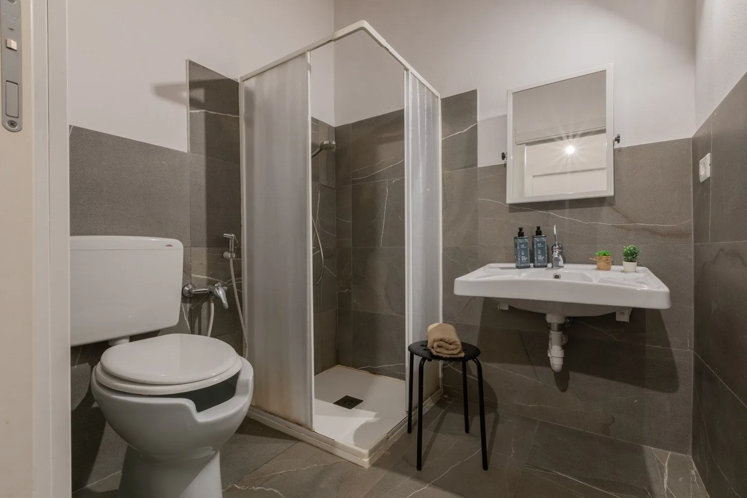 A tiled bathroom with a shower, toilet, and wall-mounted sink.