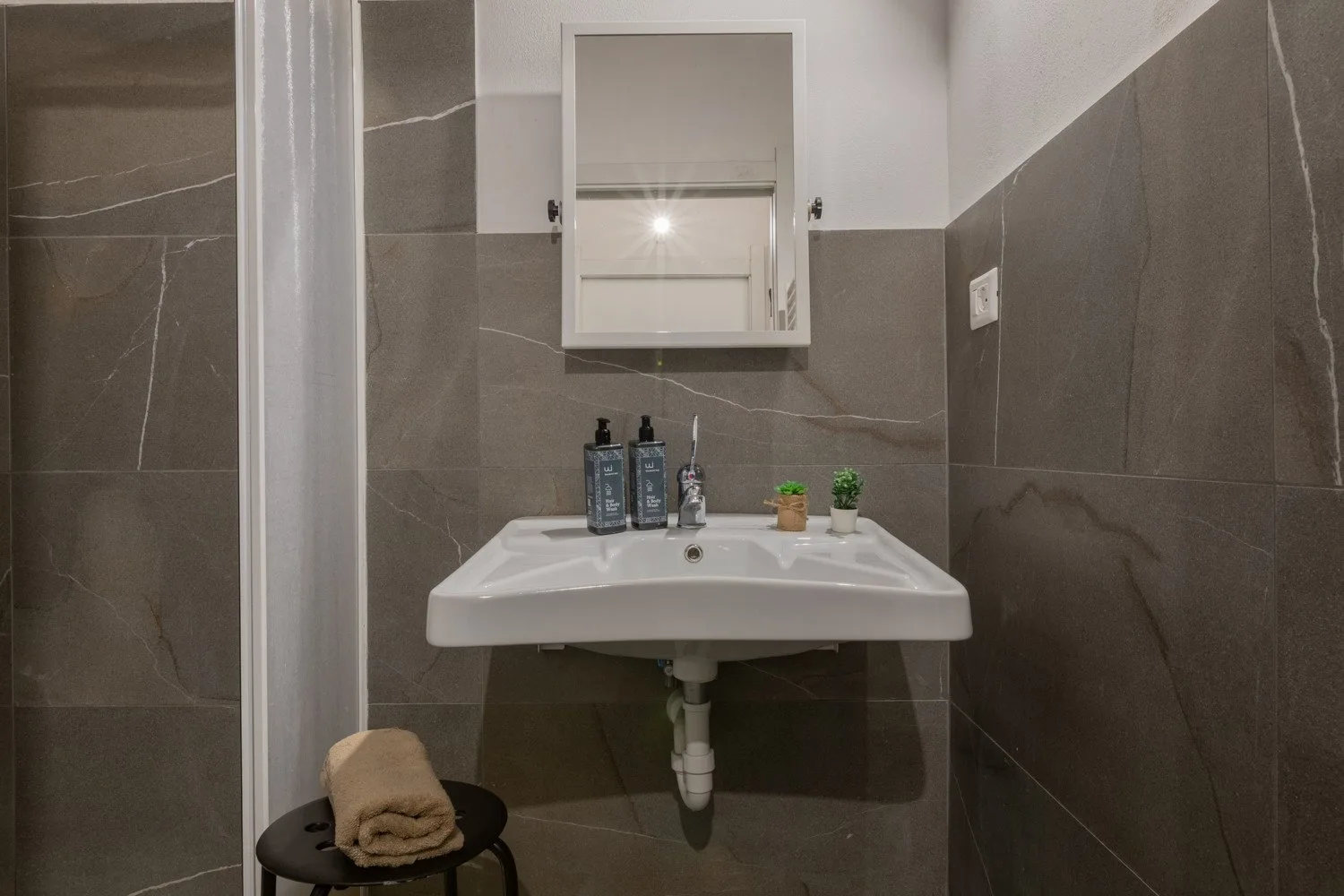 A bathroom sink beneath a mirrored cabinet, with dark tiled walls.