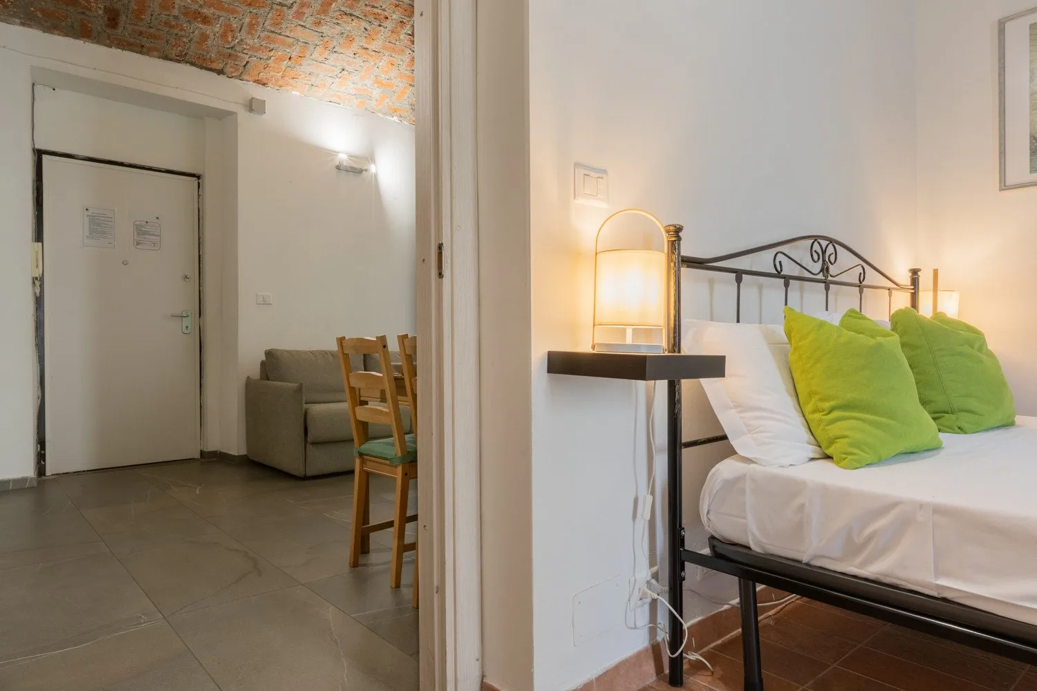 A bedroom with a metal bed frame and bright green pillows beside a small sitting area.