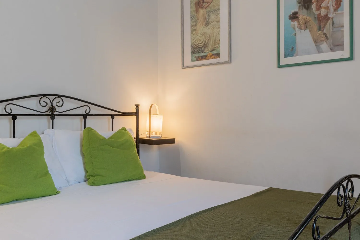 A bedroom with a white bed, green pillows, and framed artwork on the wall.