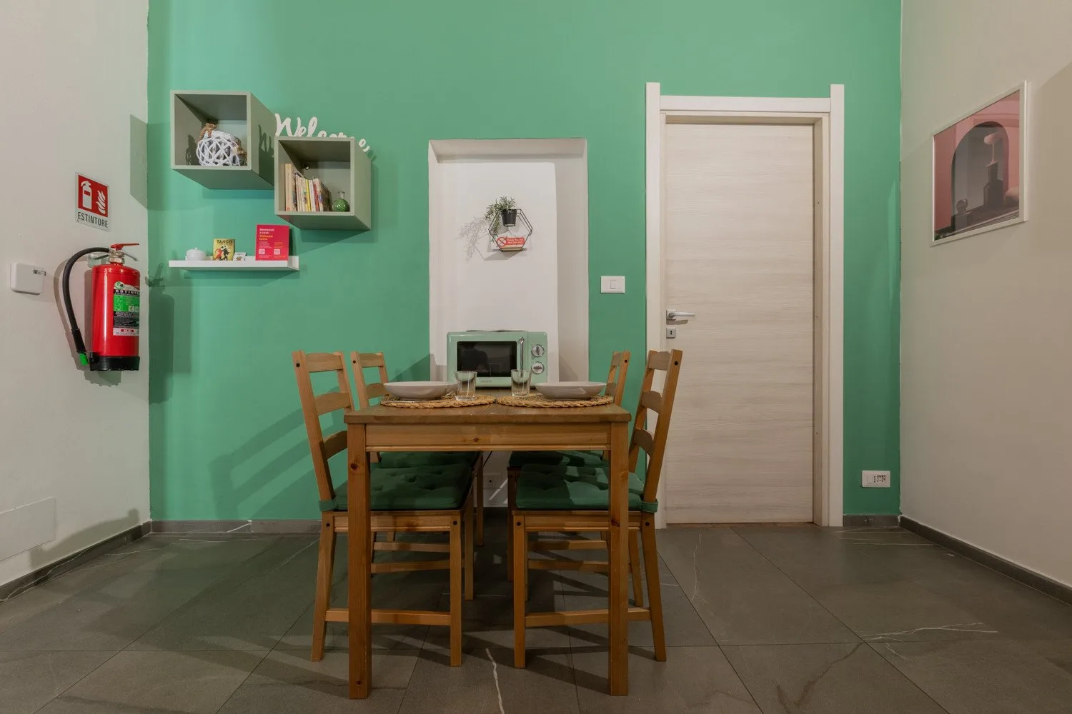 A dining area with a wooden table and chairs in front of a green wall.