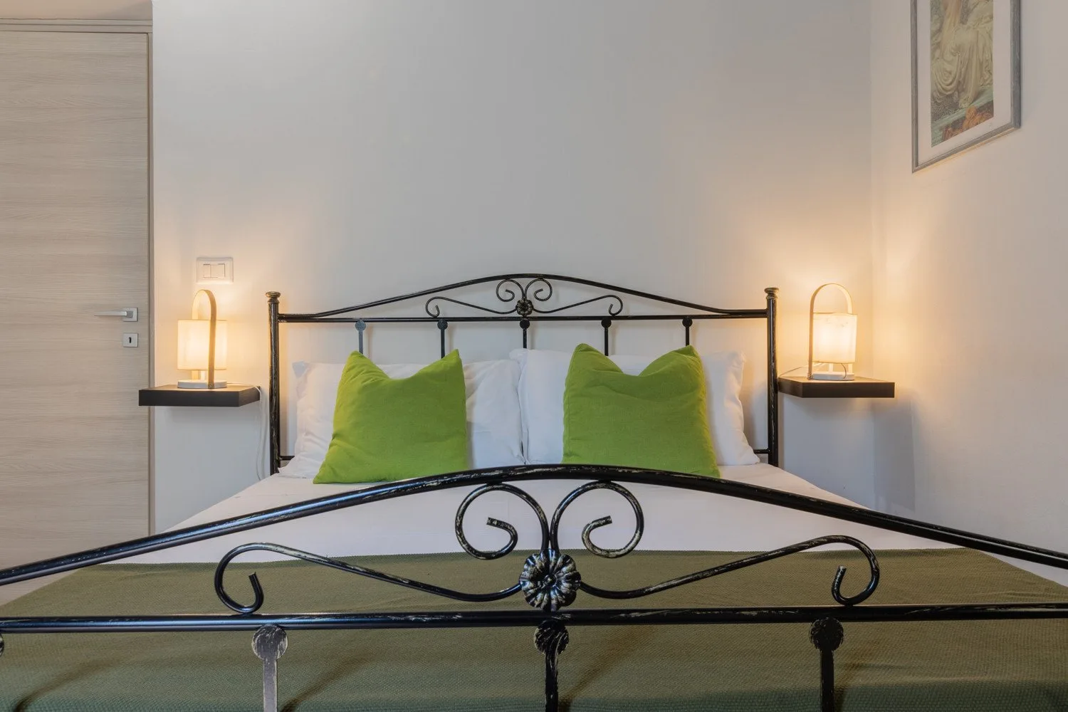A bedroom with a black metal bed, white bedding, and green accent pillows.