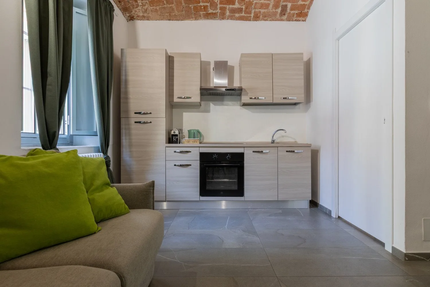 A compact kitchen with light cabinets and seating beside a curtained window.