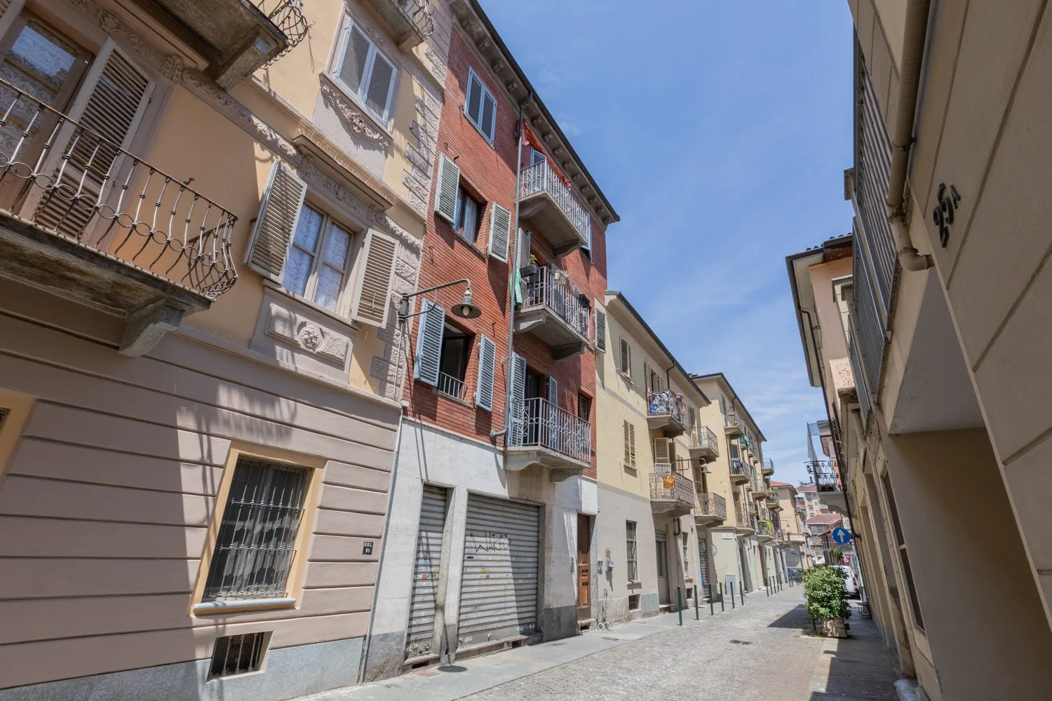 A narrow street lined with multistory buildings and balconies under a clear blue sky.
