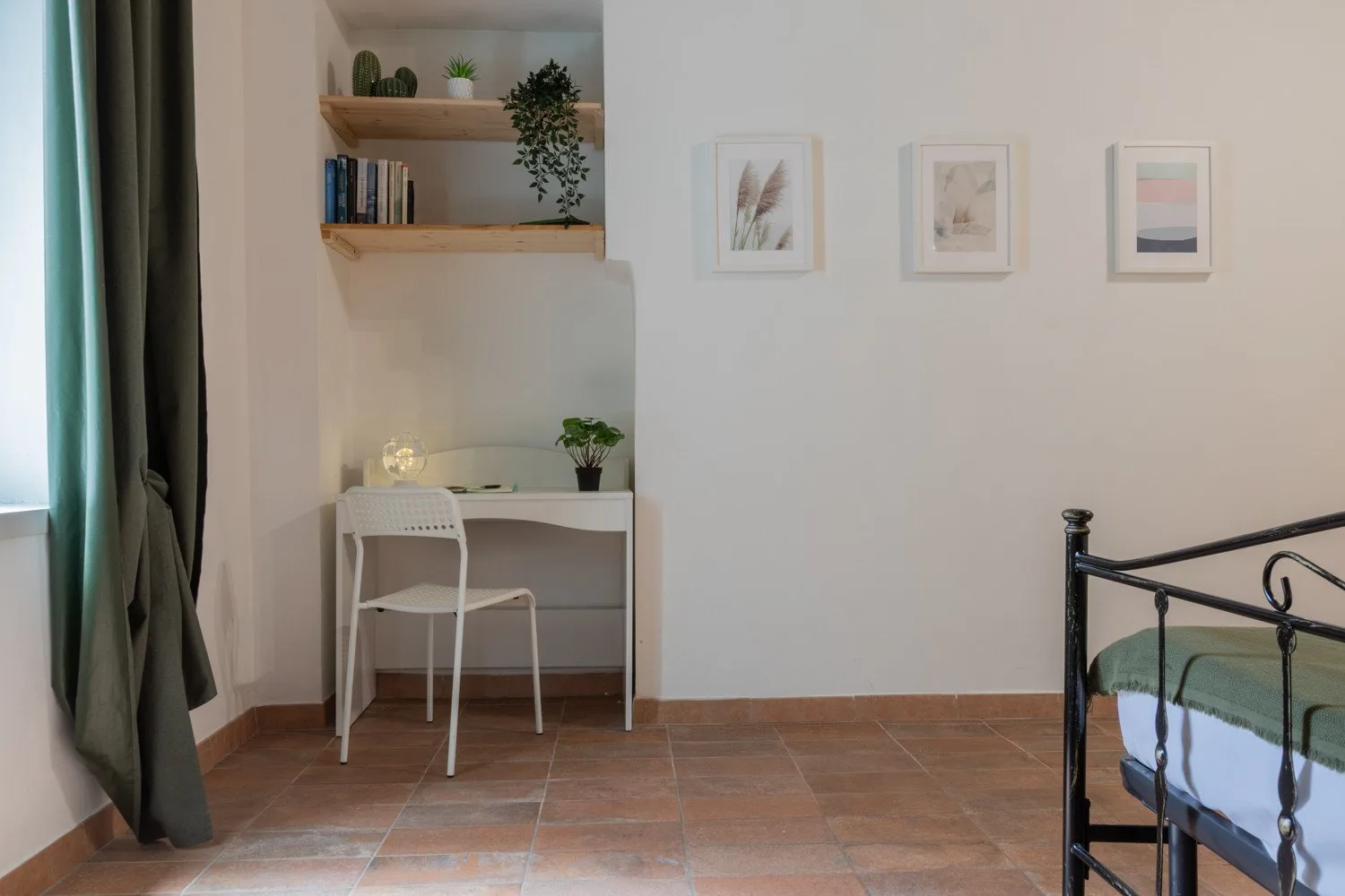 A bedroom with a desk beneath wall shelves and part of a bed.