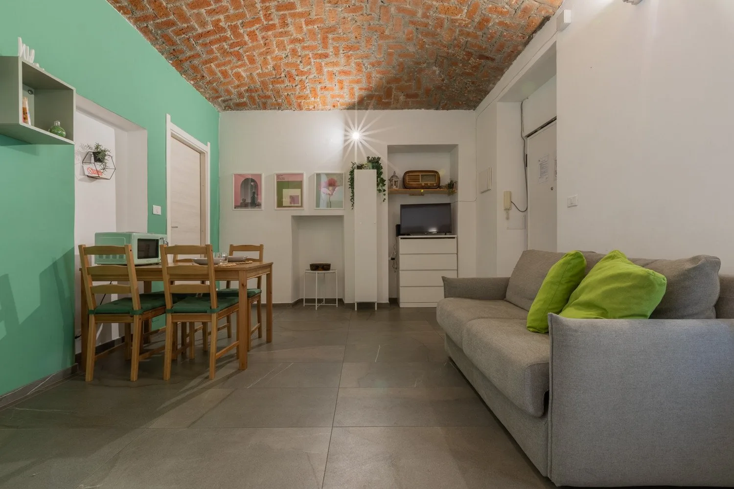 A living and dining area with a gray sofa, wooden table, and brick ceiling.