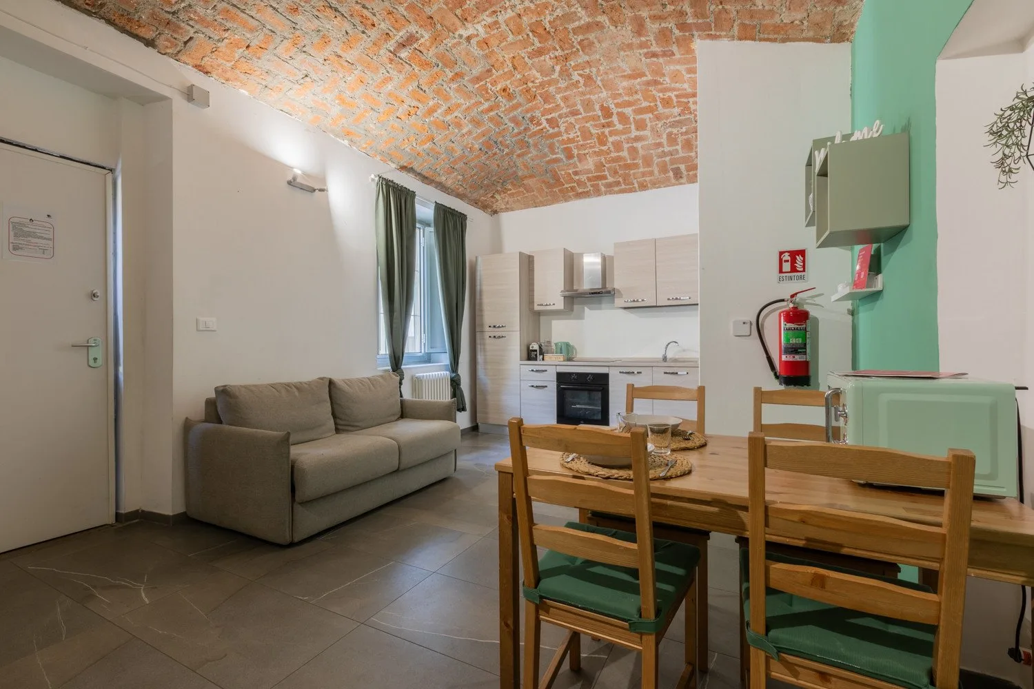 A living and dining area with a sofa, wooden table, and compact kitchen.