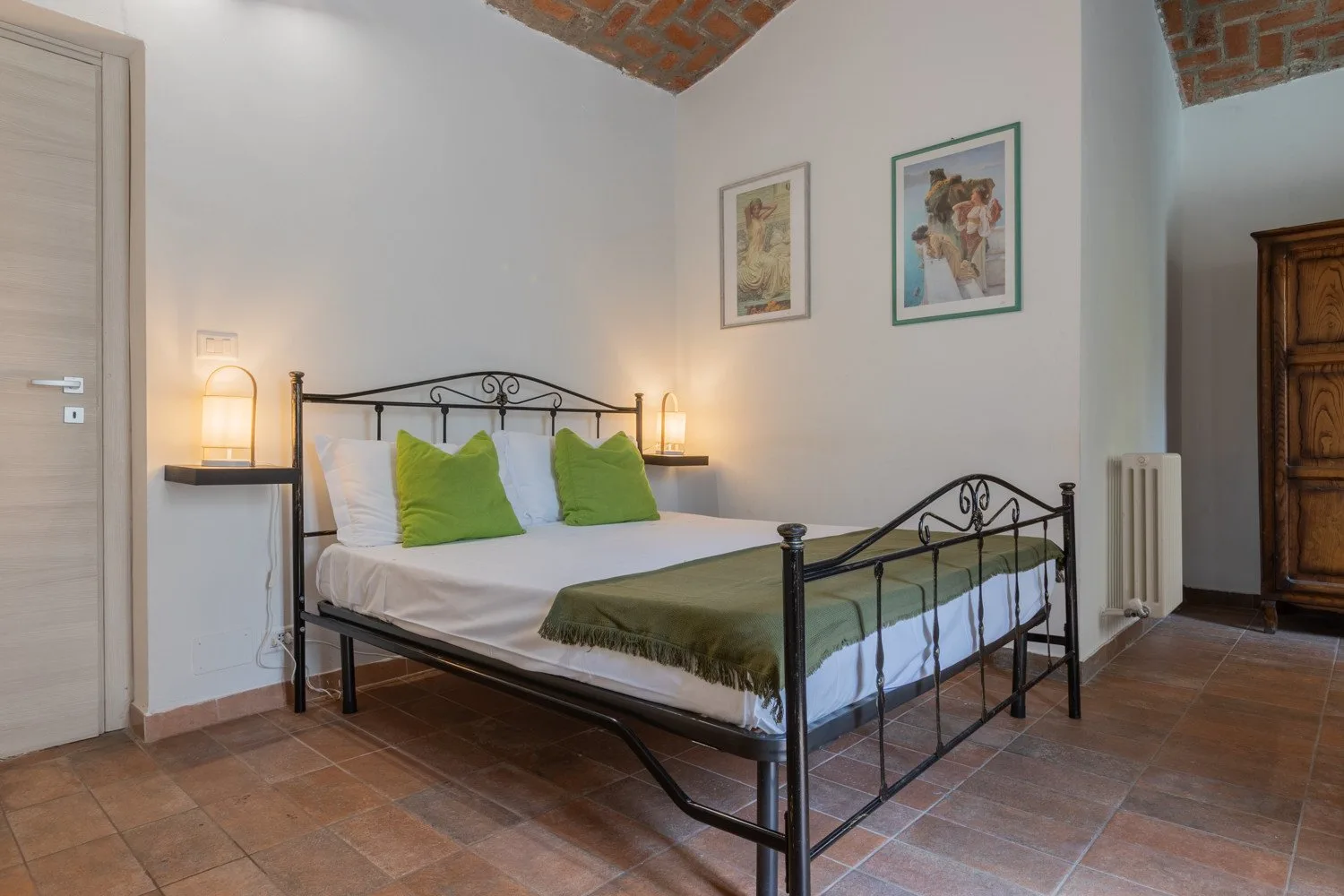 A bedroom with a metal bed, green pillows, and framed artwork on the wall.