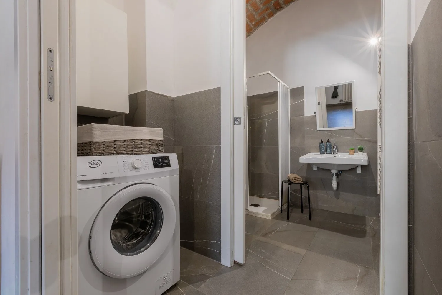 A bathroom with a washing machine and a sink beneath a mirror.